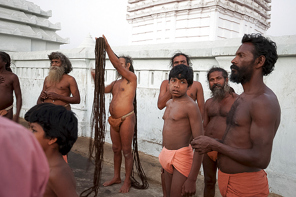 A devout Joranda monk gathers his uncut hair to coil it on top of his head, surrounded by other monks, Joranda, Dhenkanal, Orissa, India, Asia