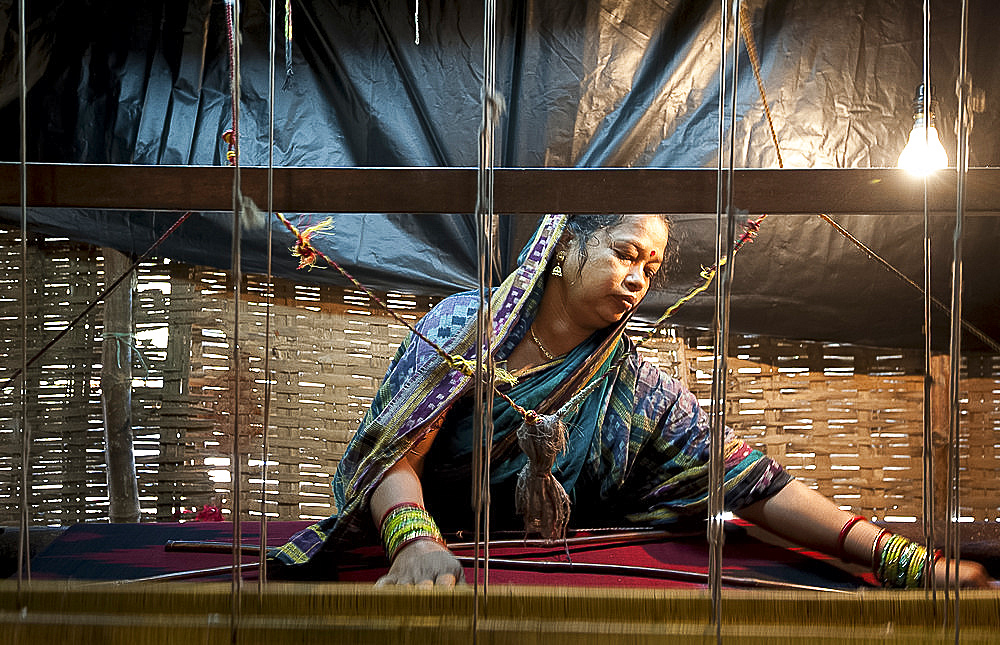 Woman in blue patterned sari weaving at loom in rough village shack, Naupatana weaving village, rural Orissa, India, Asia