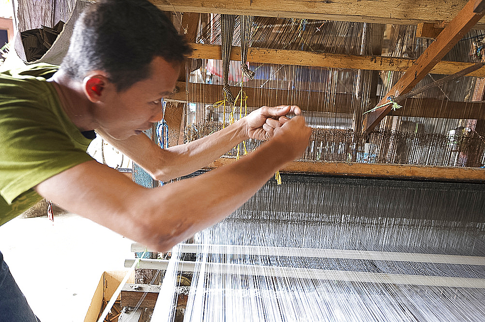 Silk weaver working to resolve a problem with a broken thread on a traditional wooden loom in a factory in Pekalongan, Java, Indonesia, Southeast Asia, Asia