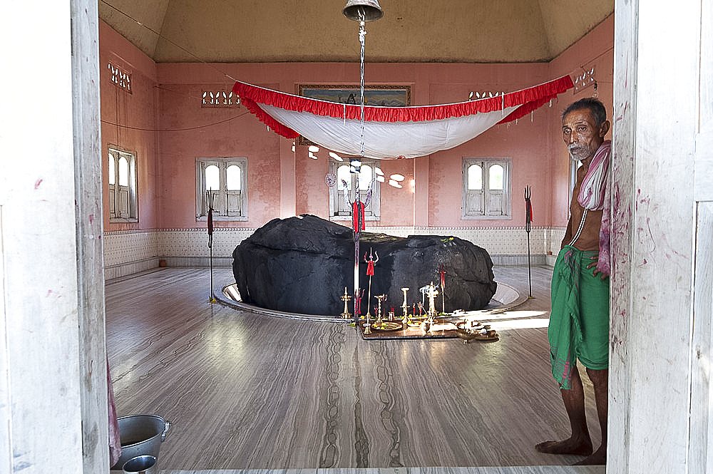 Pundit cum caretaker of holy rock from the Brahmaputra, painted black, in the village Shiva temple on the Brahmaputra riverbank, Assam, India, Asia