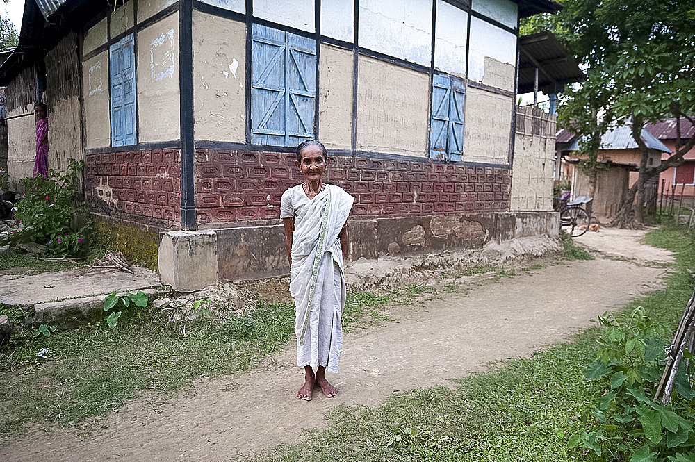 Elderly village woman outside her house wearing white sari denoting her status as a widow, Bijaynagar, rural Assam, India, Asia