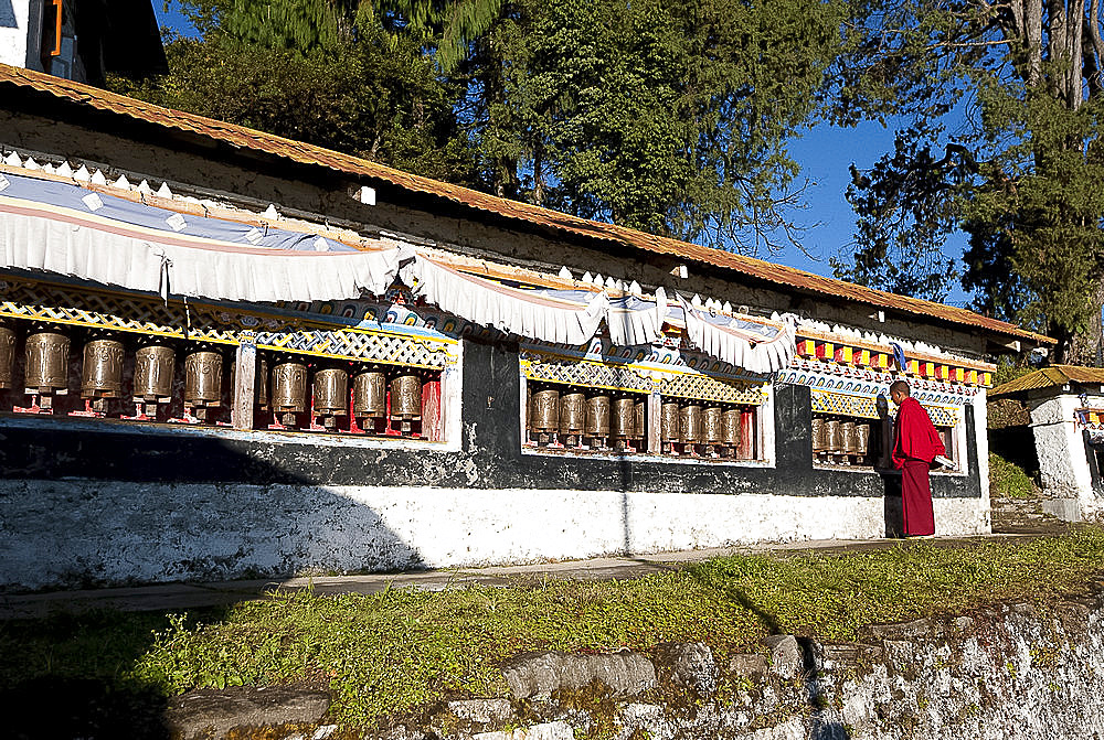 Buddhist monk in red robes turning prayer wheels in contemplative morning prayer, Tawang Buddhist monastery, Arunachal Pradesh, India, Asia