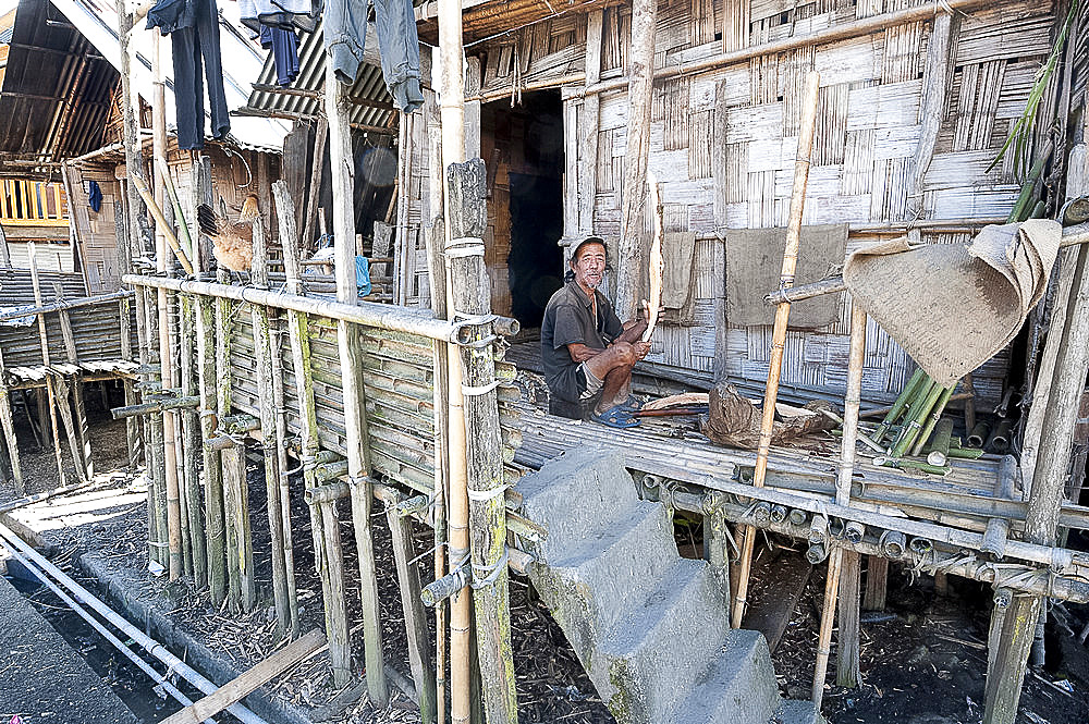 Apatani tribesman on the verandah of traditional bamboo village house, splitting wood for domestic fire, Ziro, Arunachal Pradesh, India, Asia