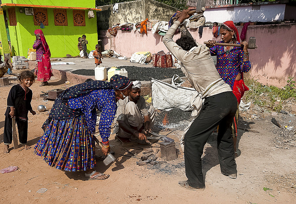 Nomadic tribal women and a man, blacksmiths, beating axe head on hot anvil in the street, Dhenkanal district, Orissa (Odisha), India, Asia