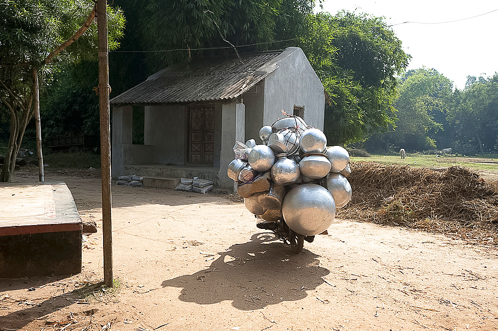 Heavily laden metal pot seller on bicycle cycling through rural village street, Dhenkanal district, Orissa (Odisha), India, Asia