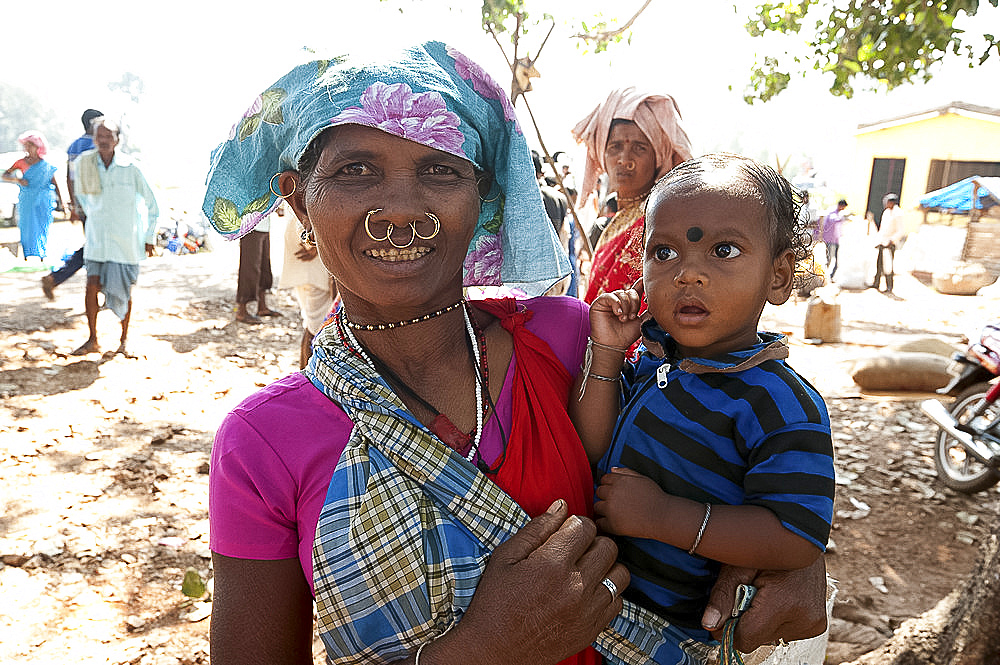 Mali tribeswoman with gold nose and ear rings carrying her son in Mali weekly tribal market, Guneipada, Orissa (Odisha), India, Asia