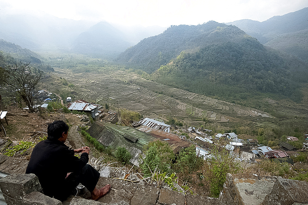 Naga man looks out from Khonoma hilltop village across Naga hills and valley ricefields, Khonoma, Nagaland, India, Asia