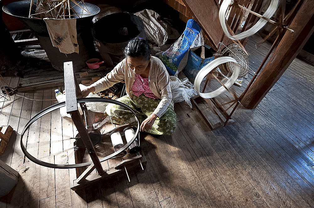 Woman spinning silk thread on a spinning wheel with bicycle wheel, Ko Than hlaing Weaving, Inpawkhan, Inle Lake, Shan state, Myanmar (Burma), Asia