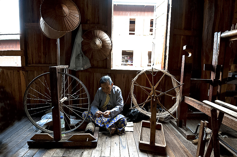 Woman spinning silk thread on a spinning wheel with bicycle wheel, Ko Than hlaing Weaving,  Inpawkhan, Inle Lake, Shan state, Myanmar (Burma), Asia