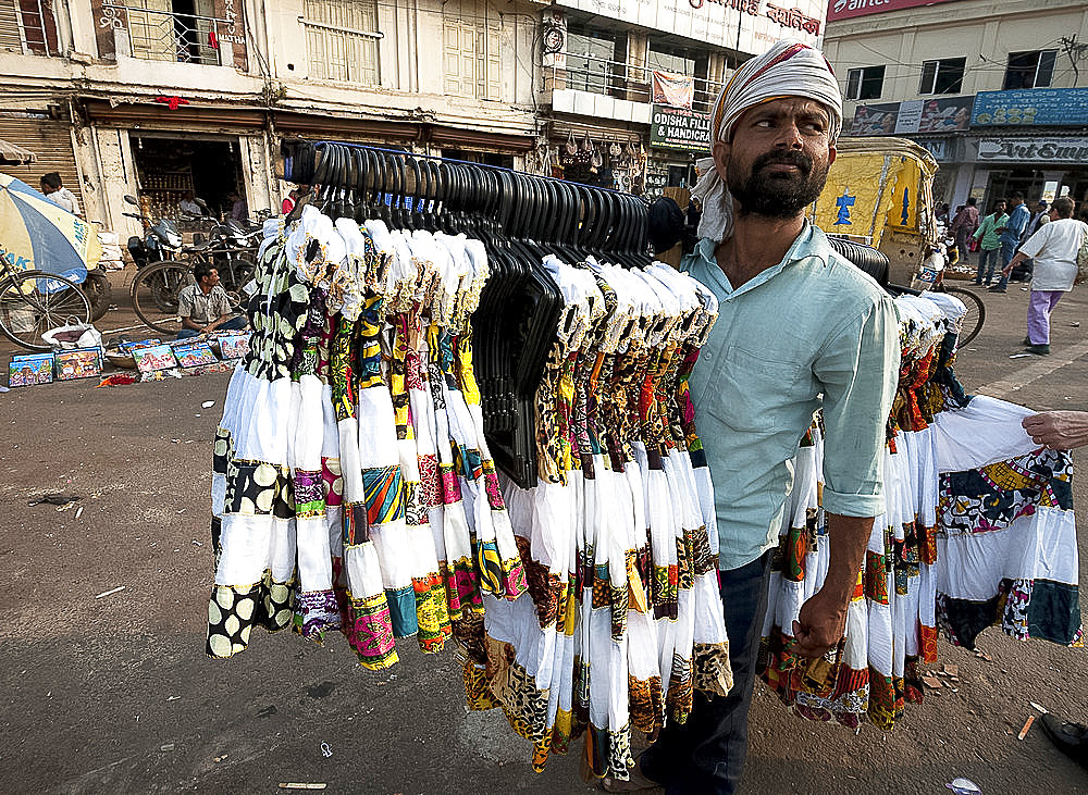 Man in head scarf selling girls' dresses from a rack he carries on his shoulder in the main street in Puri, Odisha, India, Asia