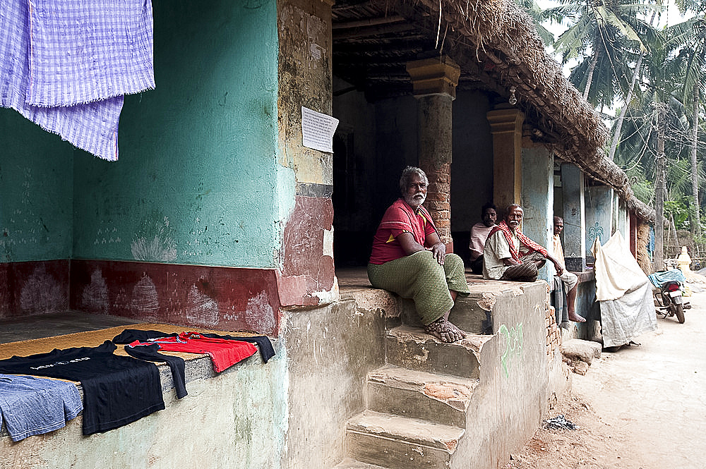 Men sitting chatting in the afternoon on the verandas of their traditional thatch and brick built village homes, rural Odisha, India, Asia