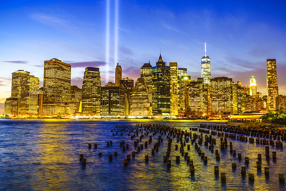 Lower Manhattan skyscrapers including One World Trade Center from across the East River at night, with light beams from the Tribute in Light 9/11 Memorial, New York City, New York, United States of America, North America