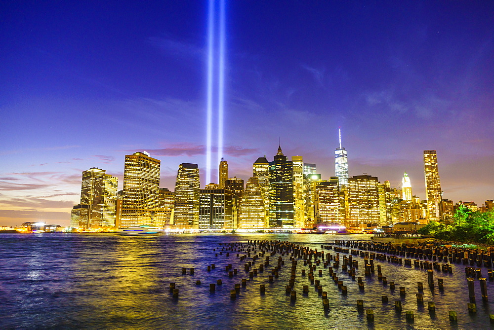 Lower Manhattan skyscrapers including One World Trade Center from across the East River at night, with light beams from the Tribute in Light 9/11 Memorial, New York City, New York, United States of America, North America