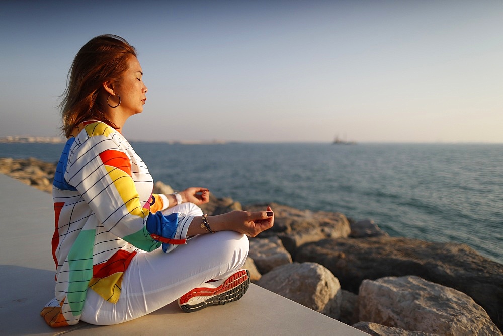 Woman practising yoga meditation by the sea before sunset  as concept for silence and relaxation, United Arab Emirates, Middle East