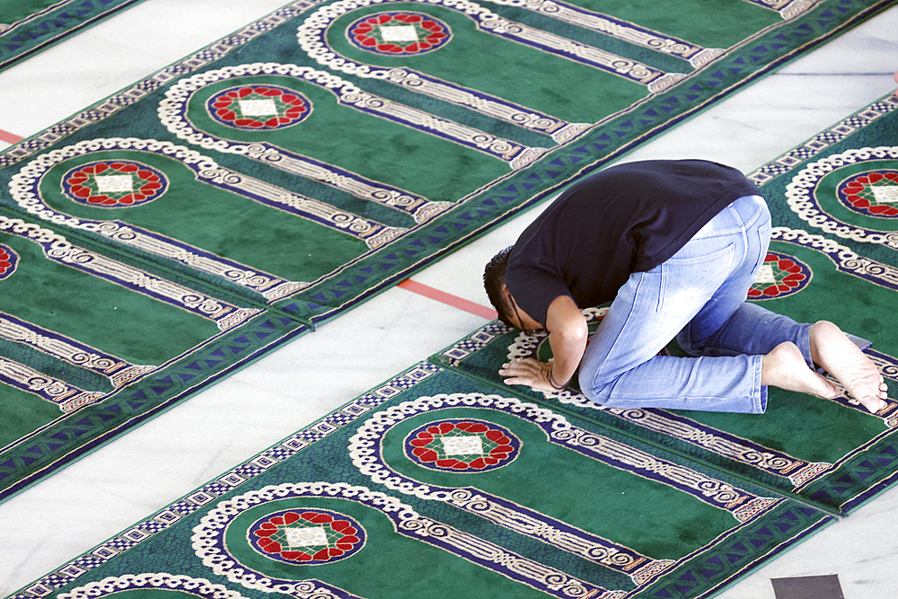 Al Akbar Surabaya National Mosque, Muslim man praying on carpet with arch design pointing towards Mecca, Surabaya, Java, Indonesia