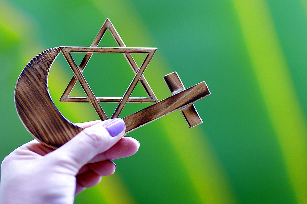 Religious symbols in hand. Jewish Star of David, Muslim star and Crescent, Christian Cross. Religion, interreligious and interfaith dialogue concept.