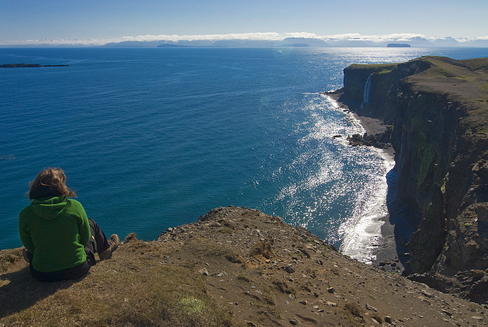 Woman sitting above the steep coast with cliffs, Vatnsnes Peninsula, Iceland, Polar Regions