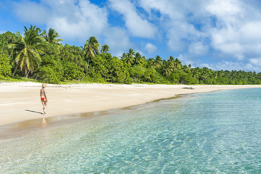 Woman walking on a palm fringed white sand beach in Haapai, Haapai Islands, Tonga, South Pacific, Pacific