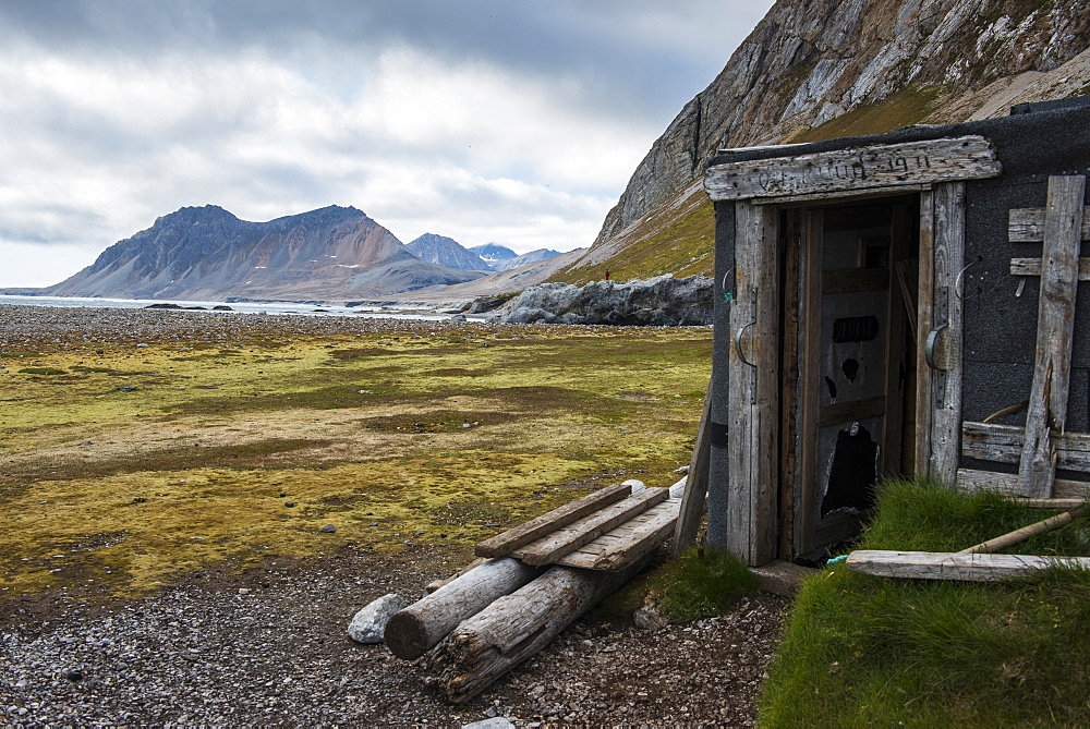 Abandoned hut on Alkhornet with a huge rock in the background, Svalbard, Arctic