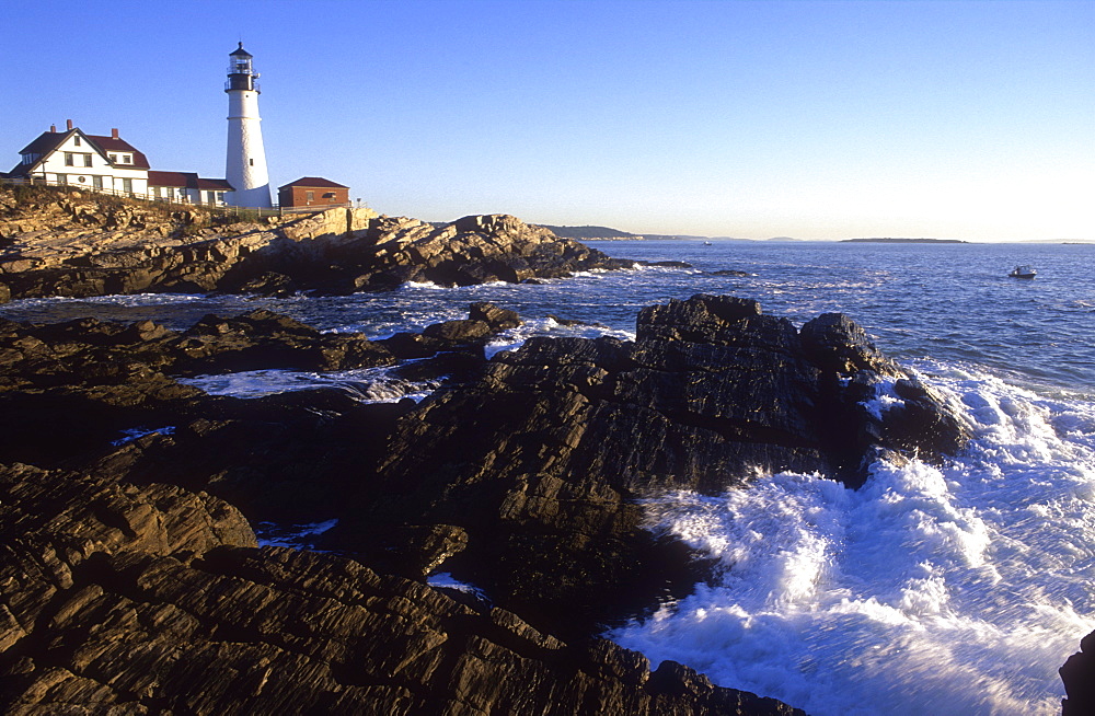 View of Portland Head Lighthouse in the early morning, with waves crashing on rocks in foreground, Cape Elizabeth, Maine, New England, United States of America, North America