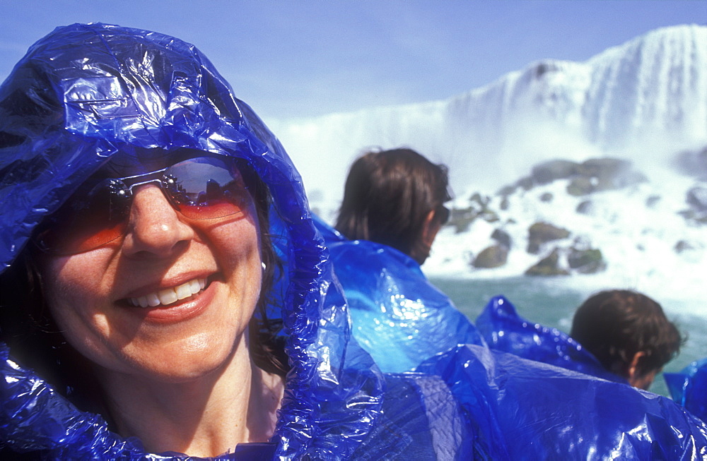 Woman smiling on board the Maid of the Mist tour boat with American Falls in background, Niagara Falls, Ontario, Canada, North America