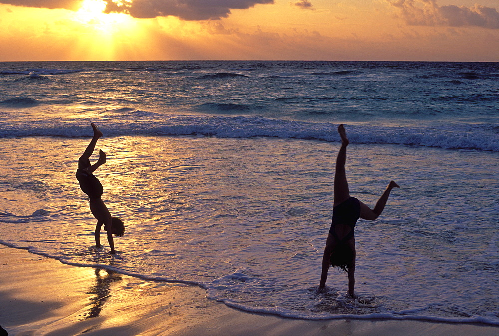 Two children playing in the surf doing hand stands at sunrise, Playa del Carmen, Mexico, North America