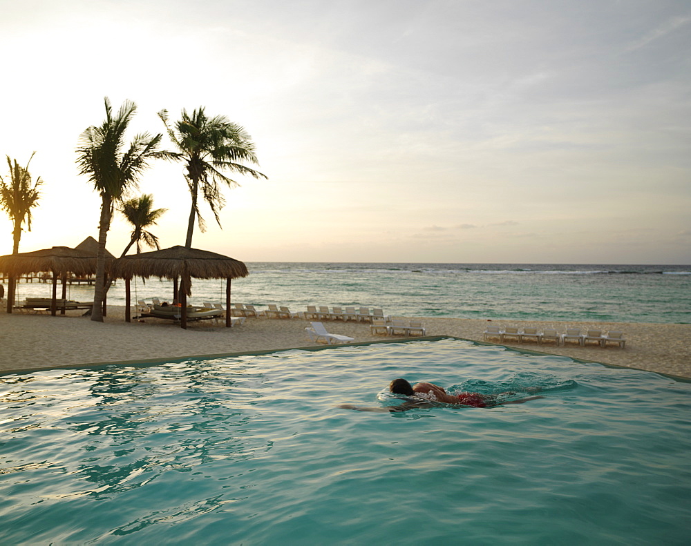 Male swimmer doing laps in an infinity pool located by the beach by the sea at sunrise, Mayan Riviera, Akumal, Yucatan, Quintana Roo, Mexico, North America