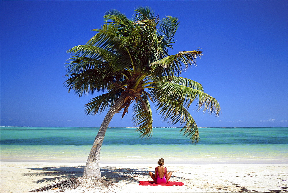 Young woman sitting under a palm tree facing the Caribbean Sea, Bavaro Beach, Punta Cana, Dominican Republic, West Indies, Caribbean, Central America