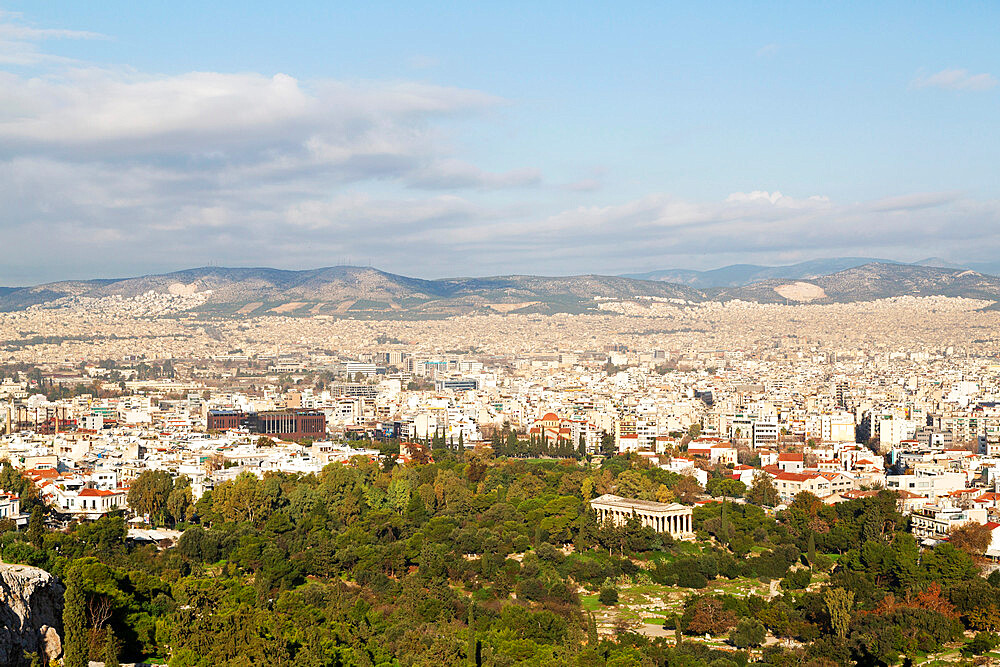 Temple of Hephaestus among trees on the ancient agora, in front of buildings of modern Athens, Greece, Europe