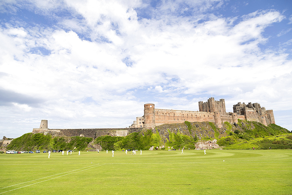 Bamburgh Castle, a medieval fortress, Grade I Listed Building constructed on top of a craggy outcrop of volcanic dolerite, overlooking a cricket ground, Bamburgh, Northumberland, England, United Kingdom, Europe