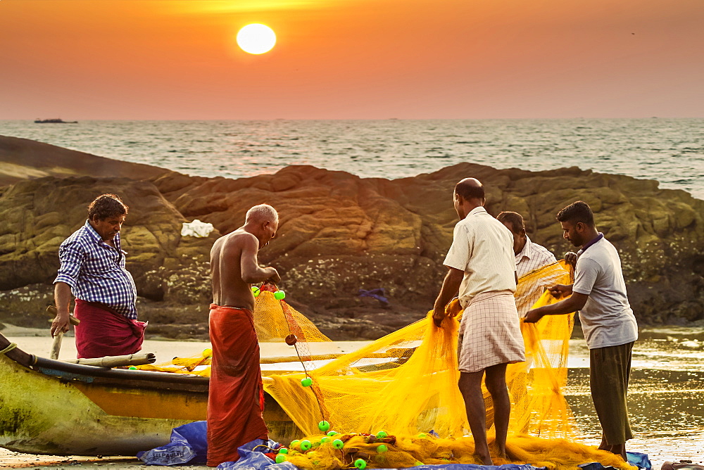 Fishermen cleaning net at sunset on lovely unspoilt Kizhunna Beach, south of Kannur on the north coast, Kannur, Kerala, India, Asia