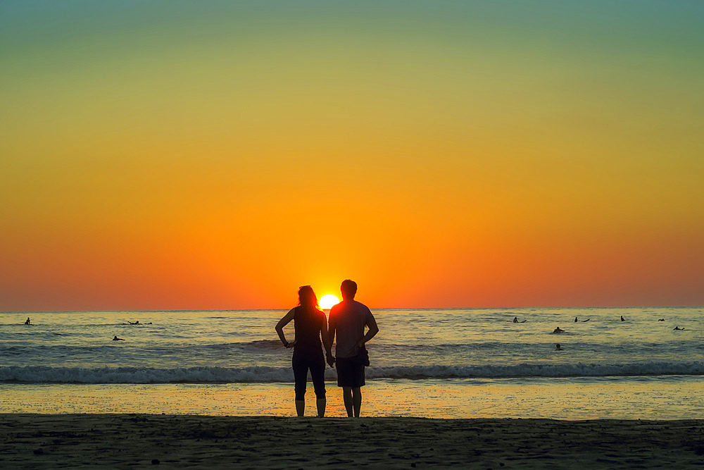 Couple hold hands on Guiones Beach where people gather to surf and watch at sunset, Playa Guiones, Nosara, Guanacaste, Costa Rica, Central America