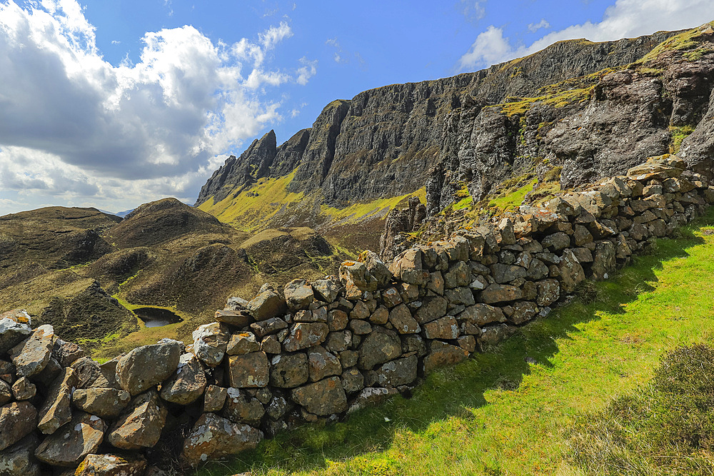 Dry stone wall and towering cliffs of basalt lava over Jurassic sediments at the Quiraing, a famous hike and scenic attraction in the far north east of the island, Quiraing, Staffin, Skye, Inner Hebrides, Scotland, United Kingdom, Europe