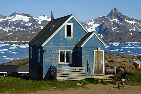 Old blue painted house in front of fjord with ice pack and snow-capped mountains Ammassalik Eastgreenland