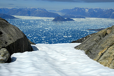 Wide open view over a snow field through rocks to icebergs in Sermilik Fjord Eastgreenland