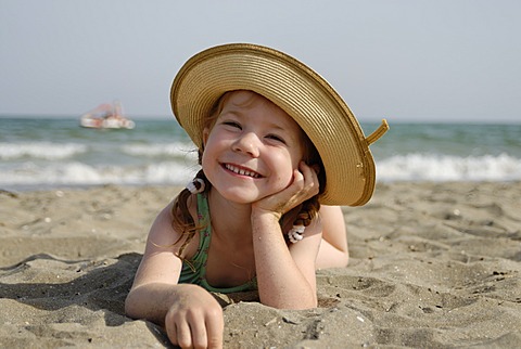 Little girl lies at a sandy beach at the sea