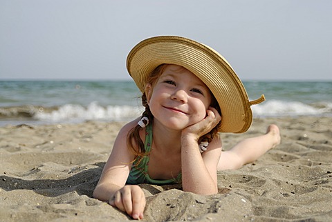 Little girl lies at a sandy beach at the sea