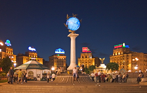 Ukraine Kiev Place of Independence people tourists visitors sit on the place with view to building of neoclassic house of labor union right and column with the world globe iluminated place with historical buildings of sowjetic realismn architectur nationa