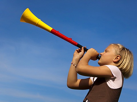 8-year-old girl blowing a trumpet in the colours of the German flag, black, red and gold, Germany