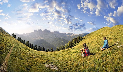 Hikers relaxing in a meadow enjoying the view of the Geisler group, Aferer Geisler mountains, Villnoesstal valley, province of Bolzano-Bozen, Italy, Europe