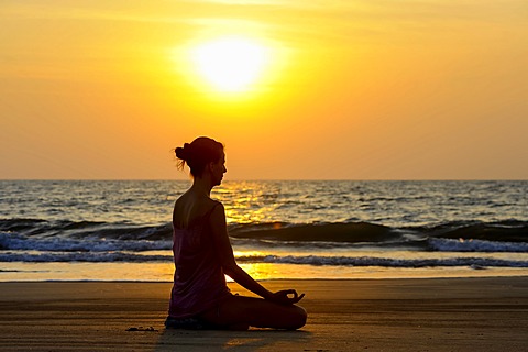 Woman meditating on a beach at sunset, Kerala, India