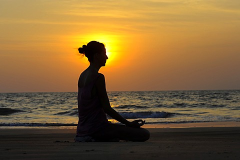 Woman meditating on a beach at sunset, Kerala, India