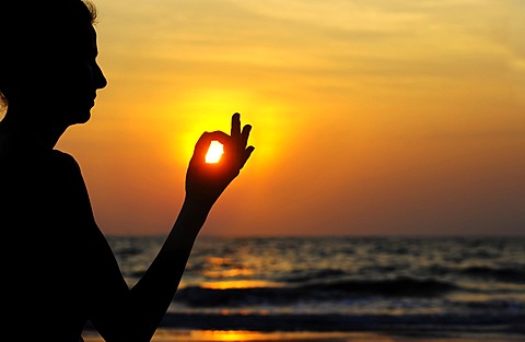 Woman meditating on a beach at sunset, Kerala, India