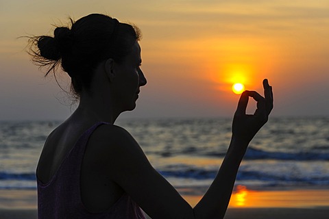 Woman meditating on a beach at sunset, Kerala, India