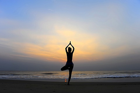 Woman doing yoga on a beach at dusk, Kerala, India