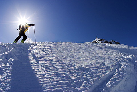 Ski touring person directly under the sun with ski sticks yellow jacket in a winter landscape wirh snow and blue sky at the Scheinbergspitze close to castle Linderhof in Germany