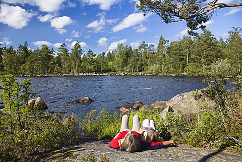 Mother and daughter resting on a big rock at St. Hindsjoen lake near Alsterbro, South Sweden, Scandinavia, Europe