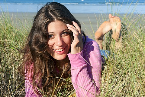 Young woman lying in the dunes on the beach, Brittany region, France, Europe