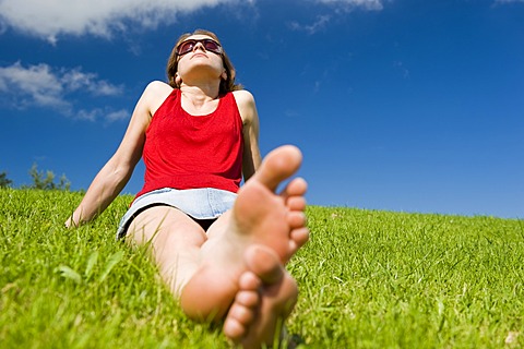 Young woman sitting barefoot in summer meadow relaxing