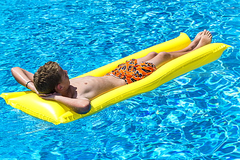 Boy, 12 years, lying on a lilo in a swimming pool